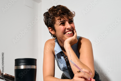 Smiling businesswoman with short hair. Hand on chin, pen in hand. She appears to be thinking or reflecting while writing.