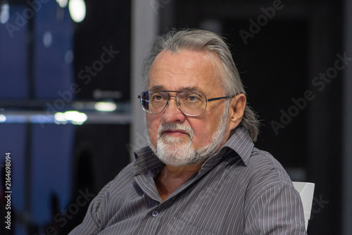 Foto Serious elderly man with glasses sitting indoors in soft light