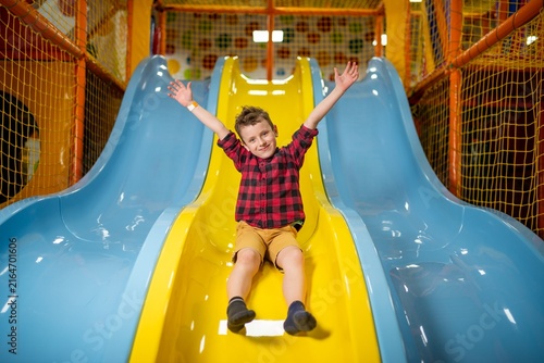 Happy boy sliding down a yellow slide indoors