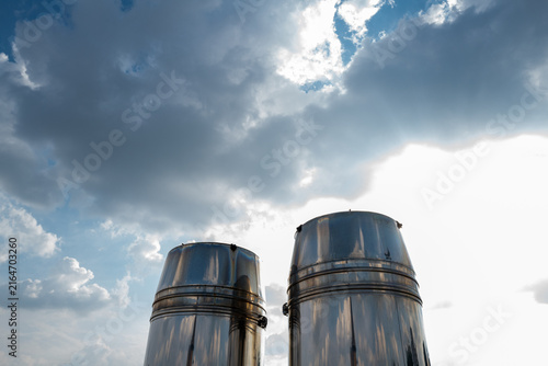 Two metallic exhaust stacks rise under dynamic sky, symbolizing industry