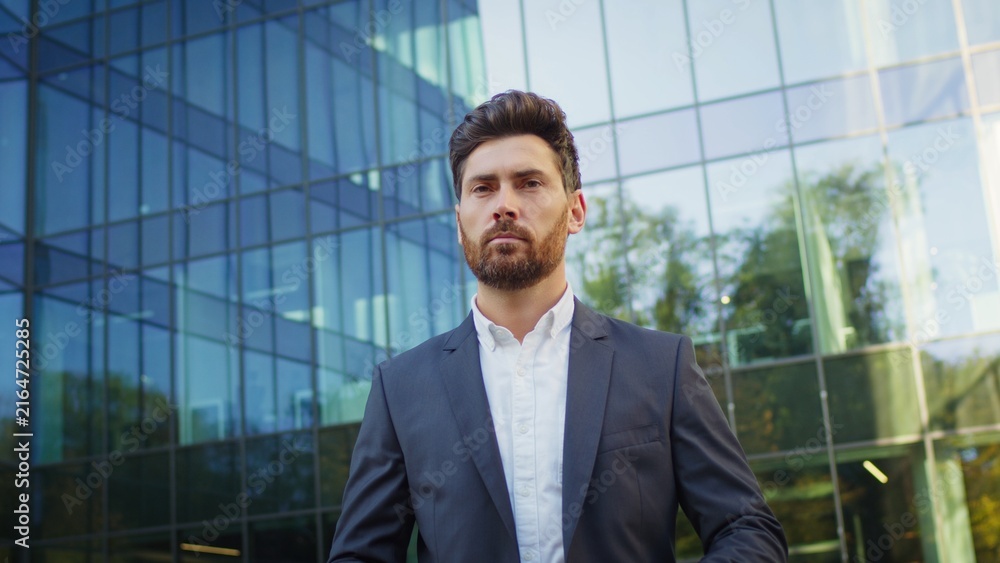 Fototapeta premium Confident businessman in a suit standing outside a modern glass office building