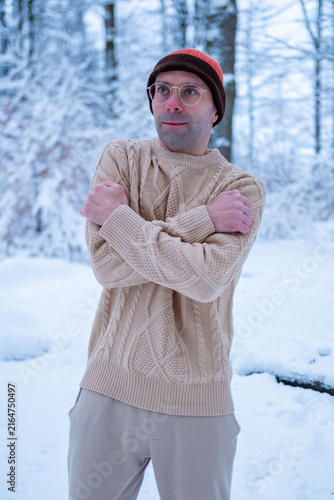 Young man in beanie and sweater shivers in snowy forest, looking lost and cold, survival struggle, winter danger, hypothermia risk, urgency rescue, Frozen and alone, freezing outdoors, lost person