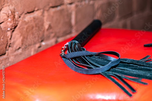 Dark leather flogger rests on bright red surface