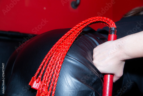 Red whip held by hand against black leather