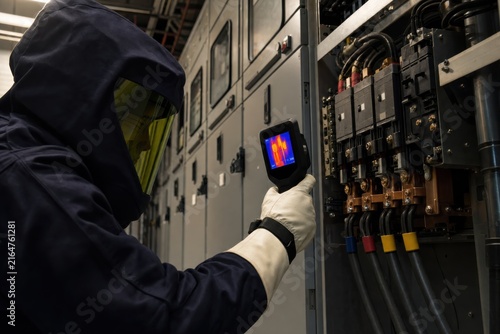 Electrician inspecting industrial switchgear with thermal camera