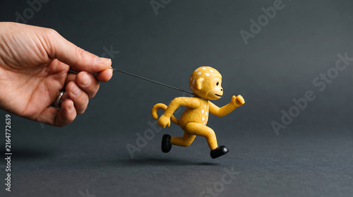 A human hand holding a string attached to a small yellow toy monkey running