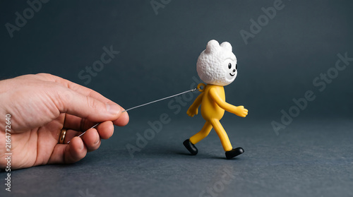 A hand pulling a small yellow cute character figurine with a string on a dark background