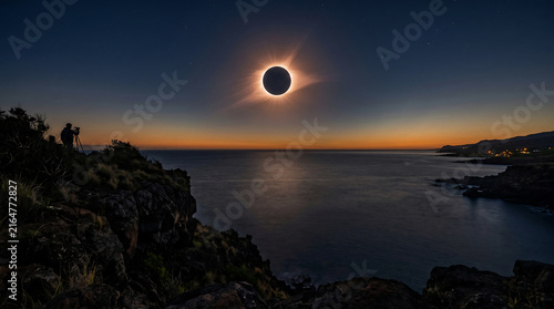A photographer capturing a total solar eclipse over the calm ocean from a rocky coastal cliffside