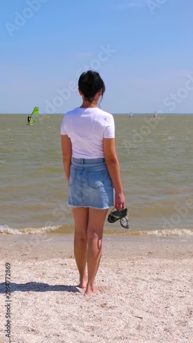 Young woman pauses at ocean shore and looks beyond horizon, embracing freedom and fresh start. Bright summer day creates uplifting atmosphere filled with confidence, possibility and independence.