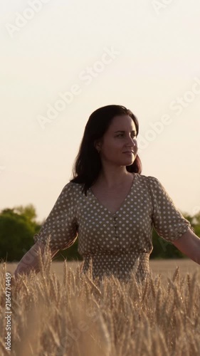 Female walks freely across golden wheat field beneath warm sunset sky. Peaceful countryside scene symbolizes freedom, hope, fresh start, optimism, personal journey and endless possibilities.