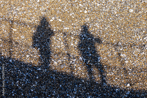 Looking down at shadows of two people on a beach,