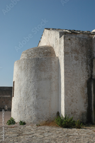 Traditional weathered whitewashed stone walls and semicircular apse of the historic Church of Panagia Myrtidiotissa stand under a clear blue sky inside Chora fortress on Kythira island