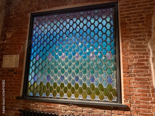 Konstfotografi Stained glass window with hexagonal pattern set against red brick wall in warm i