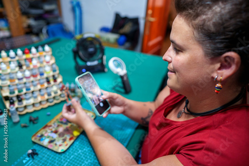 Woman recording her miniature painting process with a smartphone for social media content creation