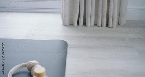 Camera is panning right, revealing beige headphones and clear water bottle on dark mat for workout