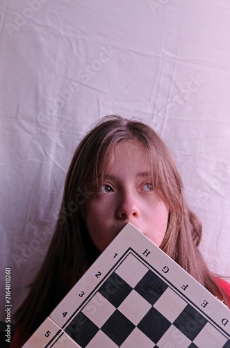 Young Teenage Girl Holding a Chessboard in a Thoughtful Pose.