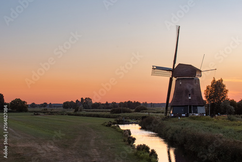 Fotografie De Kathammer windmill beside a canal at sunset