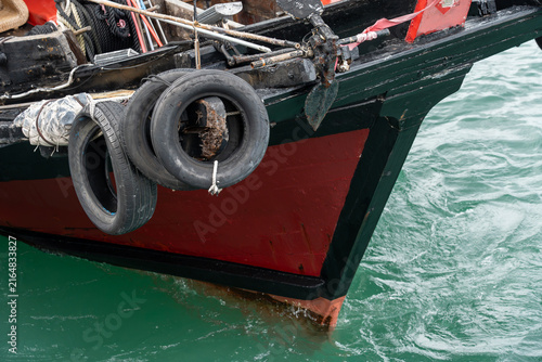 Obraz na plátně Close-up of the red and black wooden prow of a classic Chinese sampan boat equipped with rubber tire bumpers and an anchor resting in green water