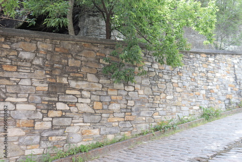 Old stone wall in the old Quebec city with a street with ancient cobblestone and vegetation and tree. Outdoor architecture with brick paving stone.