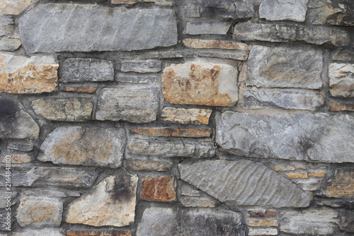 Ancient stone of a textured exterior wall with large grey and brown stones.. Construction industry and old wall repair. Abstract background with rocks on a exterior wall. Gray and brown background.