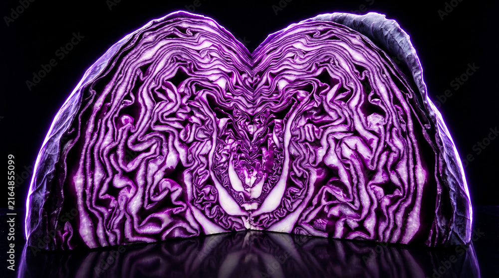 Obraz premium Cross section of fresh purple cabbage on a reflective black surface with dramatic lighting.