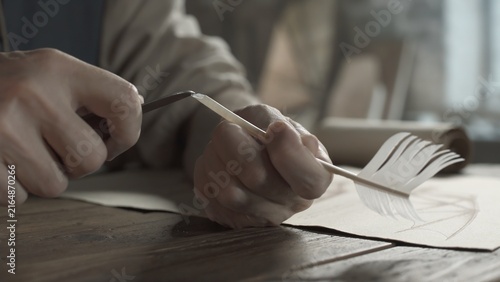 Fotografía Hands of a medieval scholar sharpening a quill pen with a penknife next to a par