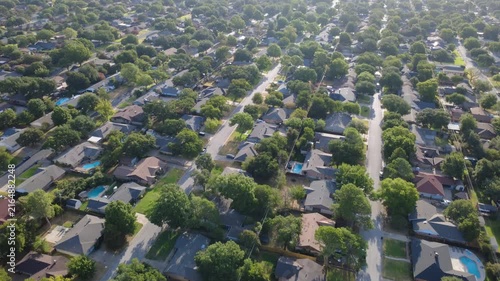 Paved residential corridors cross mature residential enclaves near Little Bear Creek. Shingled rooftops, private backyard swimming pools, dense greenery showcase suburban charm, Hurst, Texas