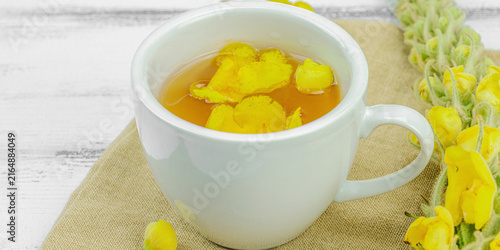 Cup of herbal tea with mullein flowers and leaves on neutral wooden background. Natural light