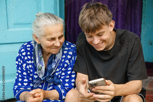 Foto Happy teenage grandson and senior grandmother looking at mobile phone screen, smiling and sharing warm family moment outside