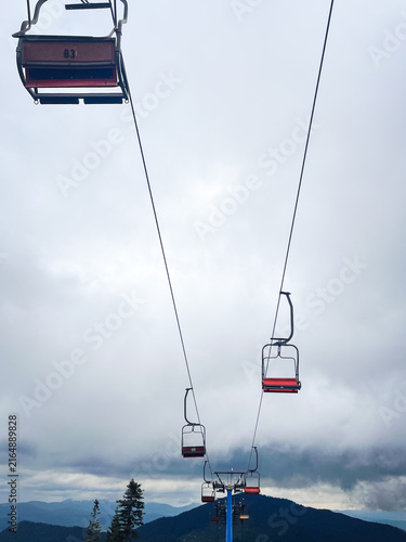 Fotografía Ski lift chairs ascend over misty mountains on a cloudy day, symbolizing travel and adventure