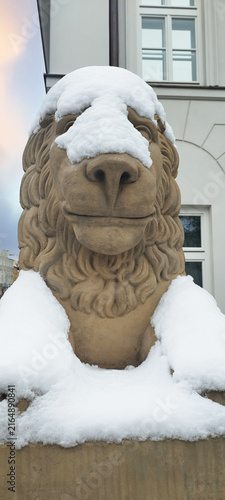 Snow covers a stone lion statue in a city, showing winter weather after a snowfall