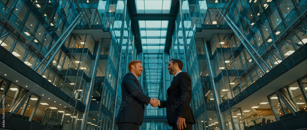 Fototapeta premium Business executives shake hands in modern office atrium, symbolizing partnership, trust, agreement, success, and cooperation.