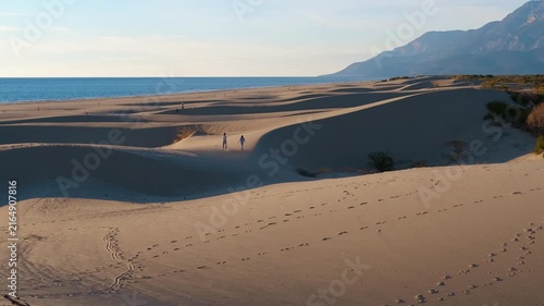 Couple walking on sandy dunes at sunset. Unrecognizable couple enjoying a romantic walk on the beautiful sand dunes of patara beach in turkey, with majestic mountains and the serene sea