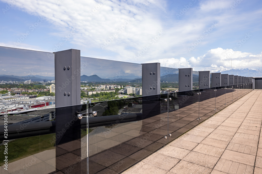 Fototapeta premium Modern rooftop balcony with glass protective barrier overlooking city and mountain landscape