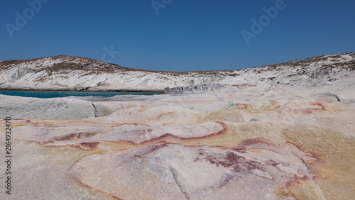 Sunlit rock formations display natural red and yellow mineral patterns near Mandrakia, Milos, Greece.