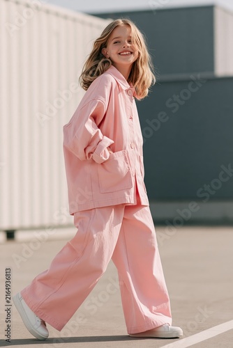 Cheerful girl walks in modern kids fashion outdoors in oversized jacket and wide-leg trousers under bright daylight Generative AI