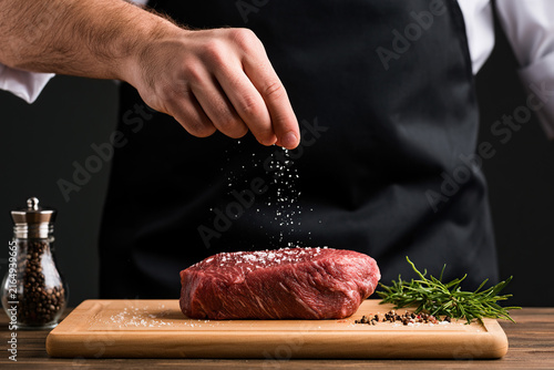 A chef's hands is salting a steak