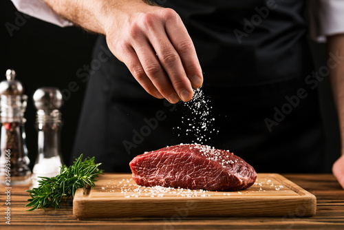 A chef's hands is salting a steak