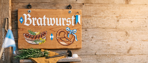 Wooden bratwurst sign with grilled sausage and pretzel illustration on rustic wall. Traditional bavarian food and Oktoberfest festival street market decoration concept