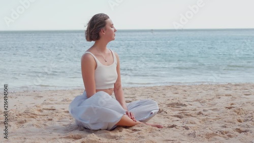 Young woman sitting in lotus pose during a meditation session on a quiet beach. Relaxation, mindfulness, and outdoor yoga concept.