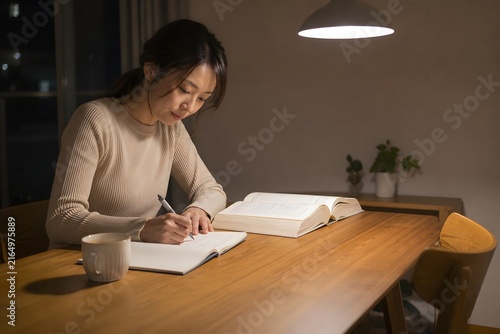 夜のテーブルで参考書を開いて書く女性