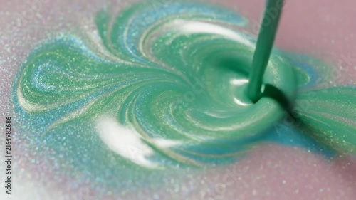 Green metallic paint swirls across a glittering surface as it gets mixed with a stick.
