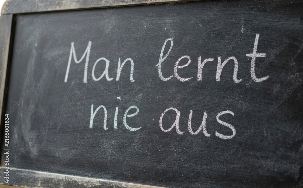 Fototapeta premium Man lernt nie aus - Deutsche Lebensweisheit auf Tafel geschrieben als Schulungskonzept