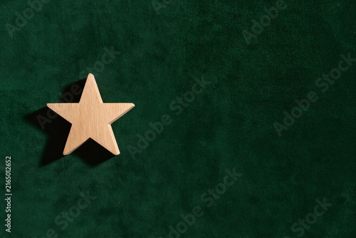 Natural wooden star on luxurious dark green velvet background, simple and elegant holiday composition with copy space.