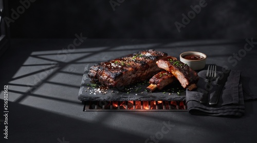 Grilled BBQ pork ribs on a hot stone plate with sauce and fork on dark background