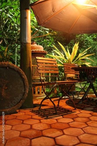 A garden bench made of a combination of wood and iron, situated in a spacious garden illuminated by the soft glow of garden lights at night.