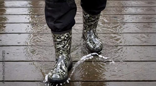 Person Wearing Camouflage Rubber Boots Standing on Wet Wooden Surface with Water Puddles