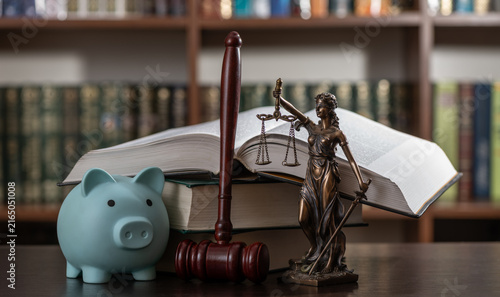 A blue piggy bank, a judge's gavel, and a figure of Themis against a backdrop of bookshelves.