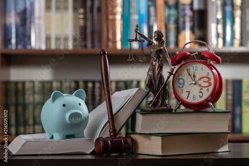 A blue piggy bank, a judge's gavel, and a figure of Themis against a backdrop of bookshelves.