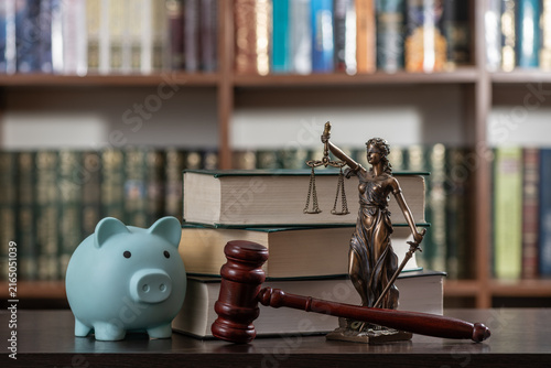 A blue piggy bank, a judge's gavel, and a figure of Themis against a backdrop of bookshelves.
